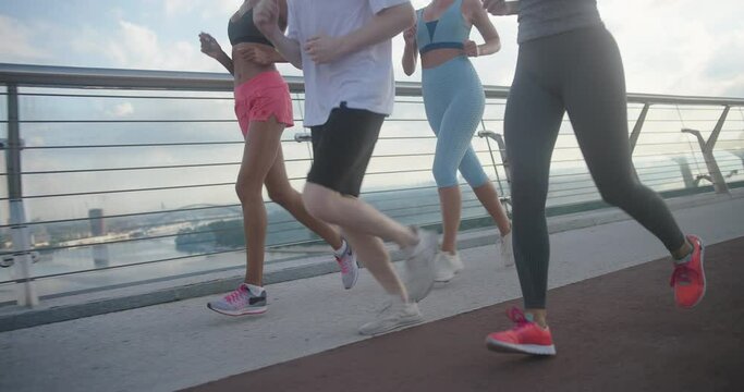 Group of athletes jogs along pedestrian brigde in morning