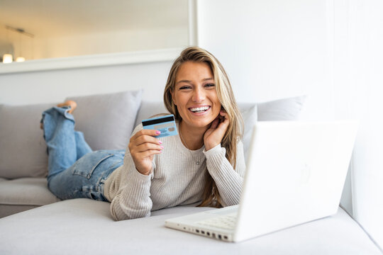 Shot of a young woman using a laptop and credit card on the bed at home. The cashless way is the convenient way. Shot of a cheerful young woman relaxing while doing online shopping