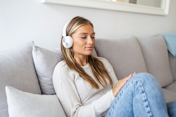 Shot of a young woman using headphones while relaxing on the sofa at home. Nothing evokes memory like music. Side view of young woman listening to music online