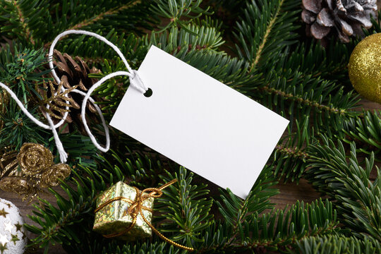 Christmas rectangle white tag mockup with white cord, close up on natural fir tree branch, with cones and Christmas decoration, Christmas sale concept. Blank paper rectangular laber product tag mockup