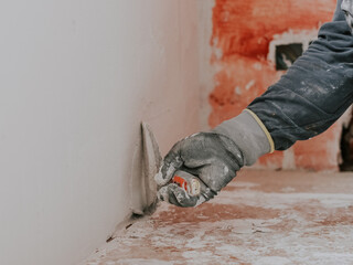 A young caucasian guy holds a spatula with white putty and plasters the wall