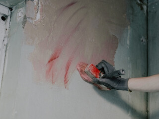 A hand of a young caucasian plasterer holds a large brush and applies a red hardening mortar