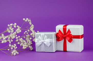 Large and small gift boxes on a purple background with a bouquet of gypsophila.