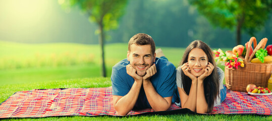Bright sunny portrait photo of young happy couple, lying together on a picnic blanket, with basket,...