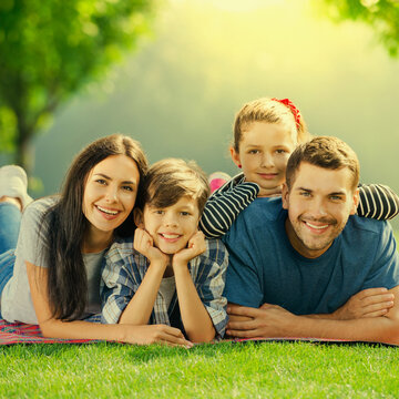 Family at Picnic. Portrait image of cheerful parents and two children, lying together on picnic blanket, at sunny day. Love, family and happy childhood concept photo.