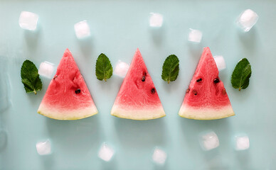 Fresh watermelon slices with ice cubes and mint leaves on a colored background.
