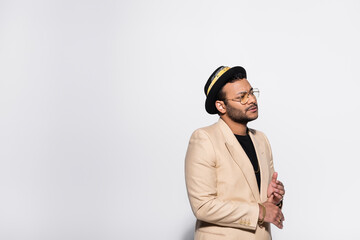 bearded indian hip hop singer in fedora hat and eyeglasses isolated on grey.