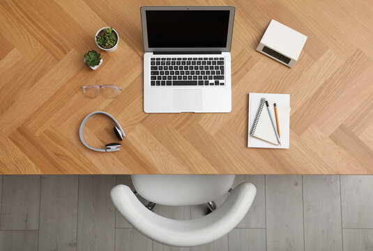 Wooden table with modern laptop near office chair indoors, top view. Comfortable workplace