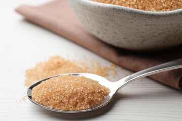 Spoon with brown sugar on white wooden table, closeup