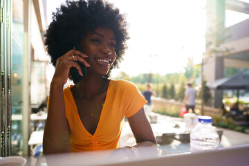 Young black woman talking on the phone while sitting in outdoor cafe
