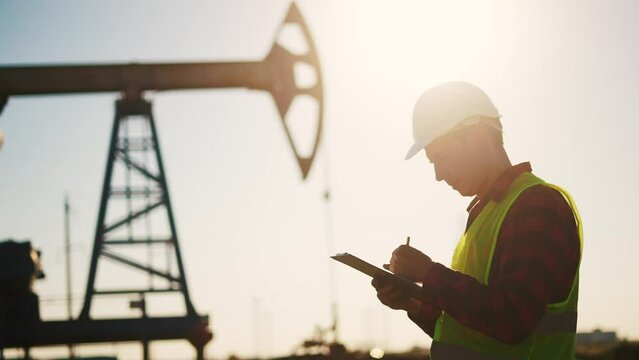 oil industry. engineer next to an oil rig signs a paper contract. oil production business finance concept. gas production. a worker oil production next an station. a worker in hard hat works sun
