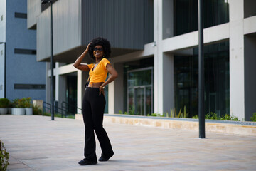 Photo of a stylish young black woman with curly hair wearing orange crop top walking in the street