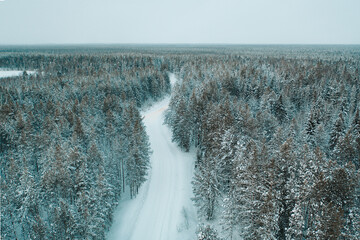 Aerial drone view of empty snowy winter road in forest