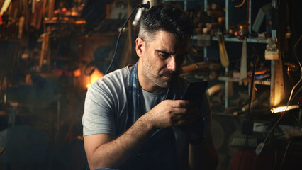 A man sitting in a garage and browsing the internet on his smartphone while relaxing after a hard workday