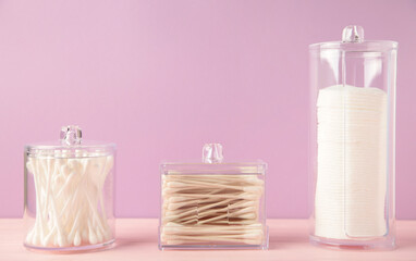 Cotton pads and cotton sticks in containers with cotton flower on purple background.