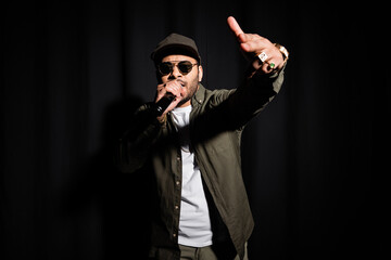 indian hip hop performer in sunglasses singing in microphone on black.