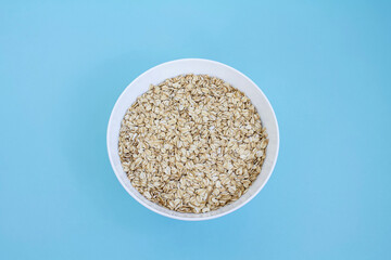 Oatmeal in white bowl on blue background, rolled oats