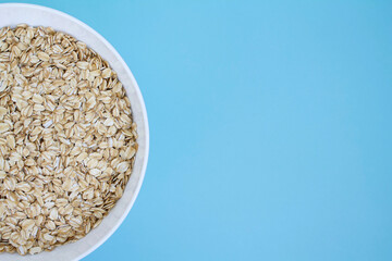 Oatmeal in white bowl on blue background with space for text, rolled oats