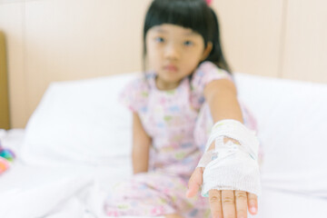 Naklejka premium Asian child admitted in hospital with saline intravenous on hand. Focus on hand.