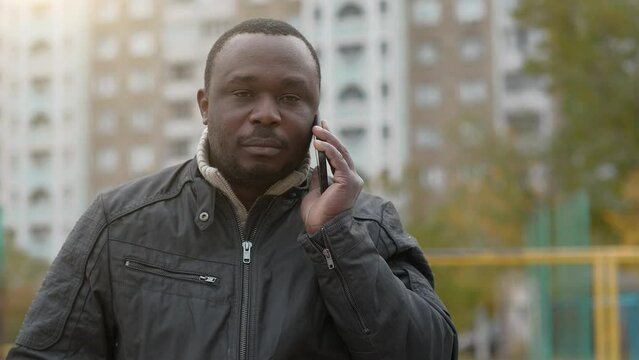 Slow Motion African american man in black jacket talks on smartphone and looks at the camera sometimes