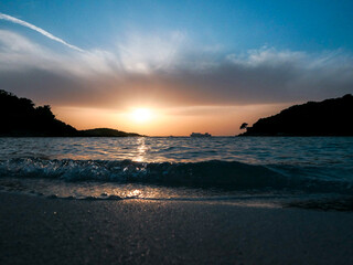 Sunset on a sandy beach with beautiful sea waves and little isles on background
