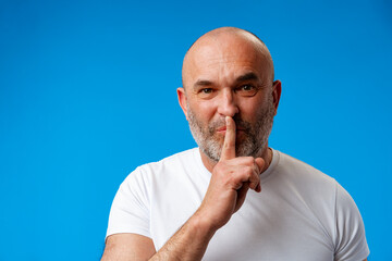 Middle age man wearing t-shirt over blue wall asking to be quiet