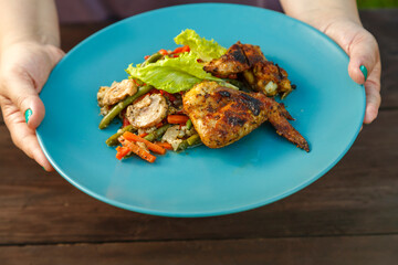 Female hands put a plate with grilled chicken and vegetables on the table on the street.