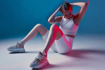 Athletic fit girl does exercise for abdominal muscles in fitness studio. Sport workout. Long exposure, modern neon light