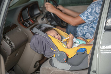 A 6 month old Asian baby girl sits on a car seat. On the seat of the car, where the father is the driver, for safety and compliance with the law. to baby and transportion concept.