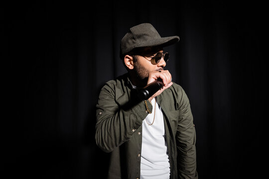middle east hip hop singer in cap and sunglasses singing into microphone on black.