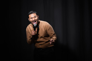 amazed indian stand up comedian telling jokes into microphone on dark stage on black.