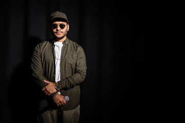 eastern hip hop performer in sunglasses holding microphone on black.