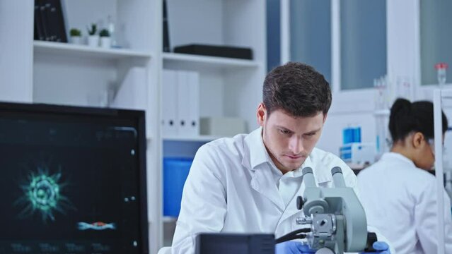 Serious clinical lab scientist studying sample virus cell under microscope