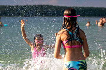 Girls having fun in lake splashing water on summer sunny hot day outdoors