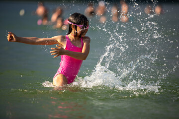 Portrait of little girl having fun in lake splashing water on summer sunny hot day outdoors