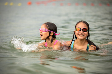 Girls sisters swimming together in water and smiling in summer