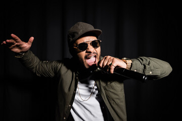 eastern hip hop singer in sunglasses singing in microphone on black.