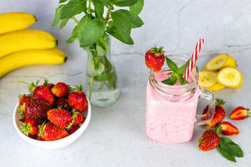 Top view of strawberry banana smoothie or smoothie garnished with strawberry berry and mint leaf on gray background.