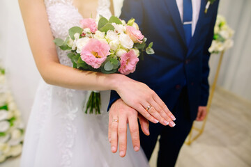 Obraz na płótnie Canvas Bride and groom in wedding costume and dress show off their gold rings. Women's wedding French neat manicure. Beautiful bouquet of white and pink roses in the hands of a young wife. High quality photo