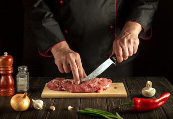 Experienced chef cuts raw beef meat on a cutting board before baking. Hotel menu recipe idea