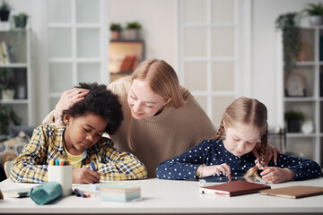 Young foster mother spending time with her adoptive children at home while they drawing at table on...