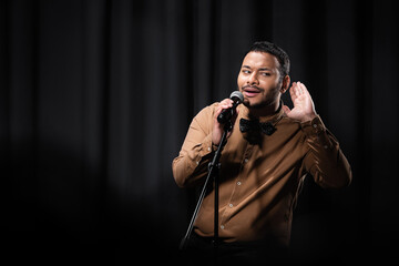 indian comedian listening during stand up comedy show on black. - obrazy, fototapety, plakaty