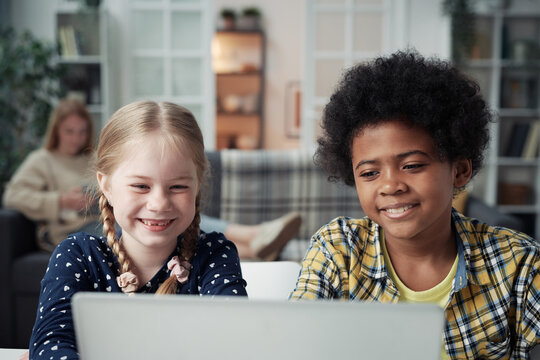 Multiethnic kids watching funny video on laptop while their mom resting in background