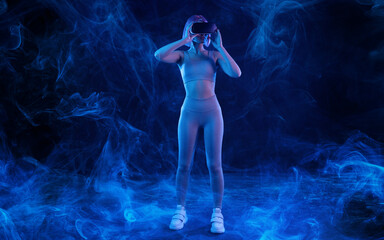 Obraz na płótnie Canvas Woman in futuristic costume. Female in modern VR glasses interacting with network while having virtual reality experience. Augmented reality game, future technology, AI concept. VR. Neon blue light.