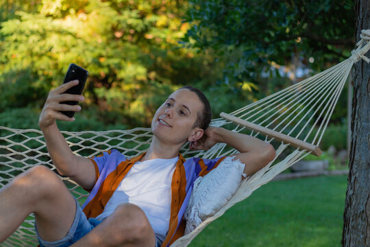 Young handsome man taking a selfie while laying in a hammock in the afternoon in summer time