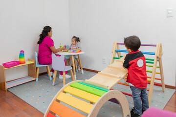 Introverted boy, looks from afar at a pediatrician doctor who plays with a girl, at a table