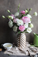 Fototapeta na wymiar A beautiful bouquet of white lisianthus and pink peonies in a vase on a table with a linen napkin. Seasonal summer flowers.