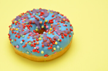 colorful donut with blue icing on on a yellow background close up