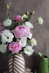 A beautiful bouquet of white lisianthus and pink peonies in a vase on a table with a linen napkin. Seasonal summer flowers.
