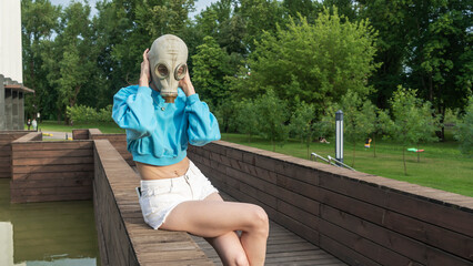 A girl in a gas mask sits by the fountain. Alienation in the city. Fashion, ecology and loneliness concepts.